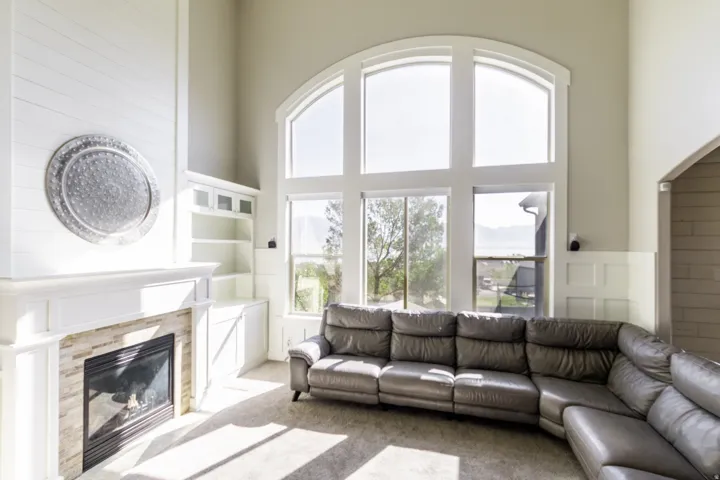 Two-story great room featuring a gas fireplace with a stacked stone surround, custom built-in cabinetry, and large arched windows