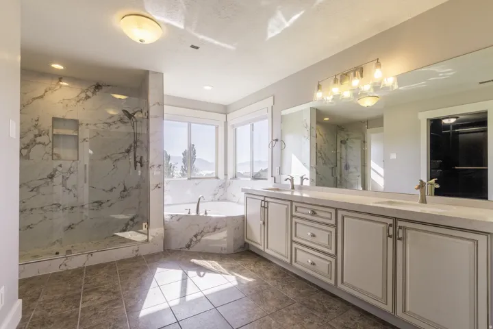 Dual vanity with undermount sinks, frameless glass shower enclosure, built-in soaking tub, tile flooring, and multiple windows