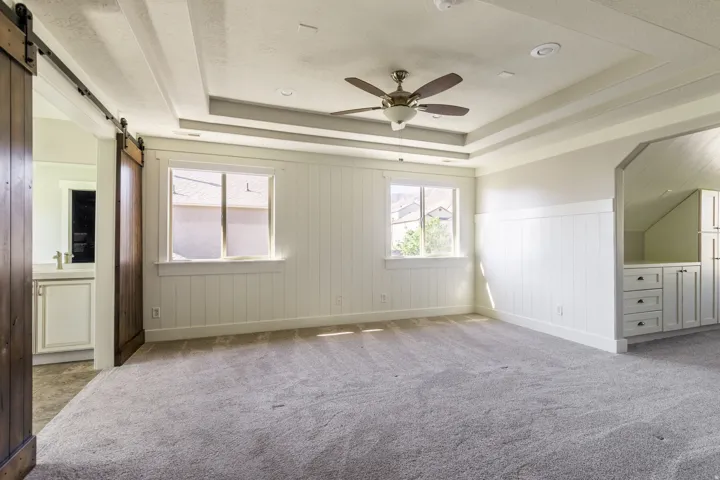 This primary suite features a tray ceiling with a ceiling fan, shiplap wall accents, built-in cabinetry, and a barn door