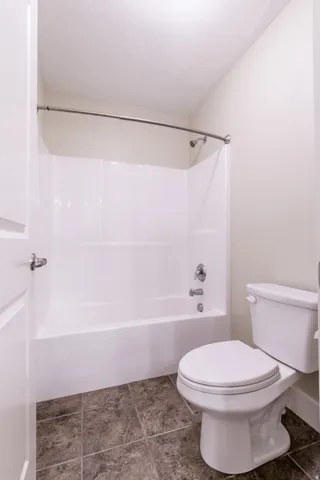 White tub and shower combination with chrome fixtures, curved shower rod, and dark tile flooring