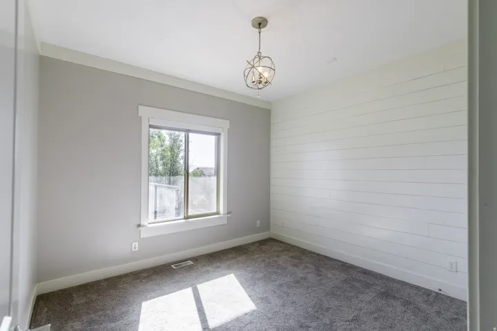 White shiplap accent wall, gray carpet flooring, single window with white trim, and a decorative ceiling light fixture