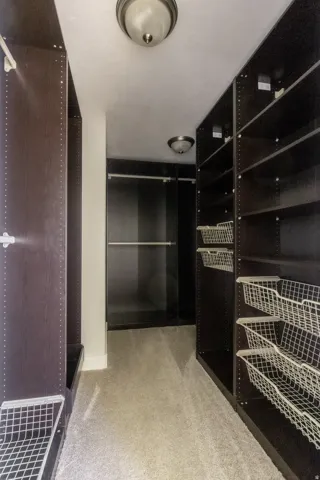 Walk-in closet featuring built-in dark wood-finish shelving, wire storage baskets, and flush-mount ceiling lighting