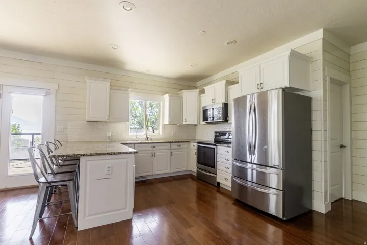Kitchen featuring white shaker cabinetry, stainless steel appliances, wood-finish flooring, and a white subway tile backsplash