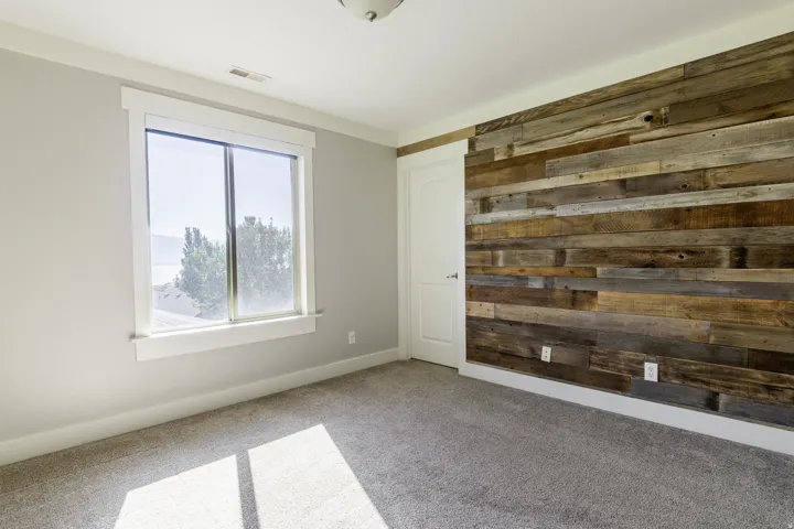Textured wood-panel accent wall, neutral-toned carpeting, white trim, and a white interior door with a silver-tone handle