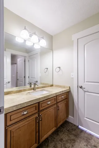 Wood-finish vanity with a single basin sink, stone-finish countertop, and brushed nickel faucet