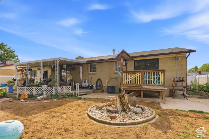 Rear exterior featuring an expansive covered patio, elevated wood deck, and a circular rock garden