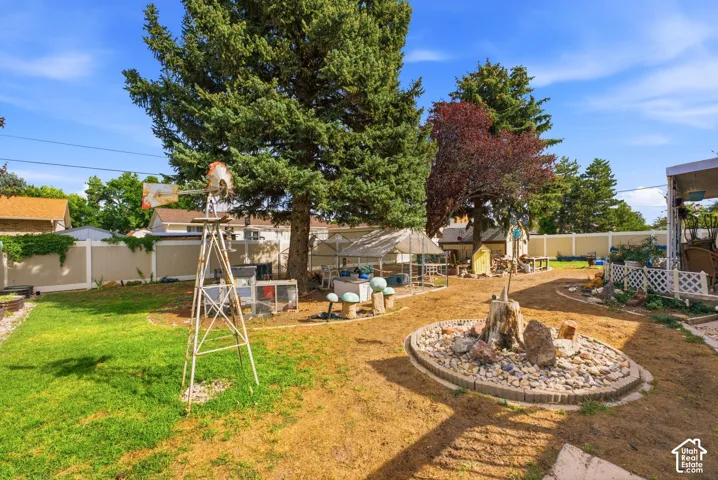 Expansive backyard featuring mature trees, a decorative windmill, a rock garden, and perimeter fencing