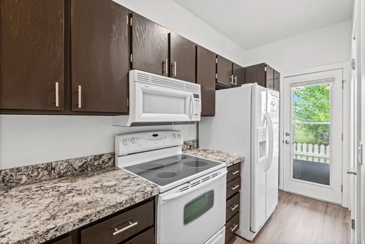Fully renovated kitchen featuring dark wood cabinetry, white appliances, granite countertops, and LVP flooring.