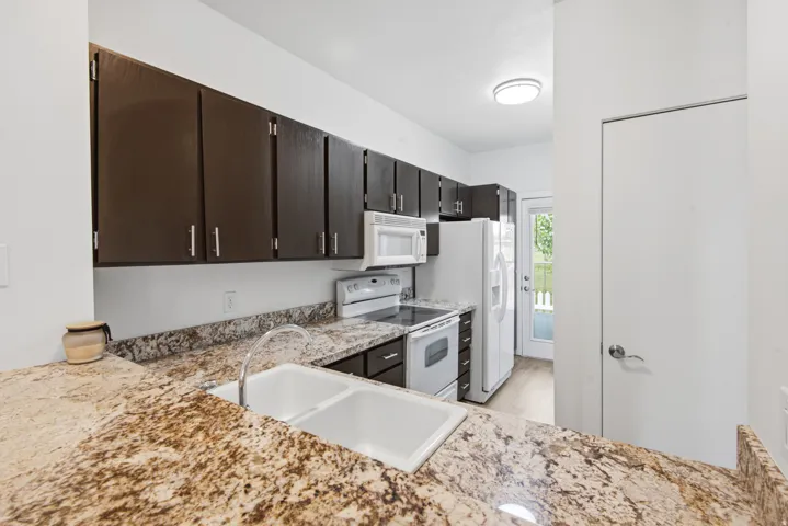 Fully renovated kitchen featuring dark wood cabinetry, white appliances, granite countertops, and LVP flooring.