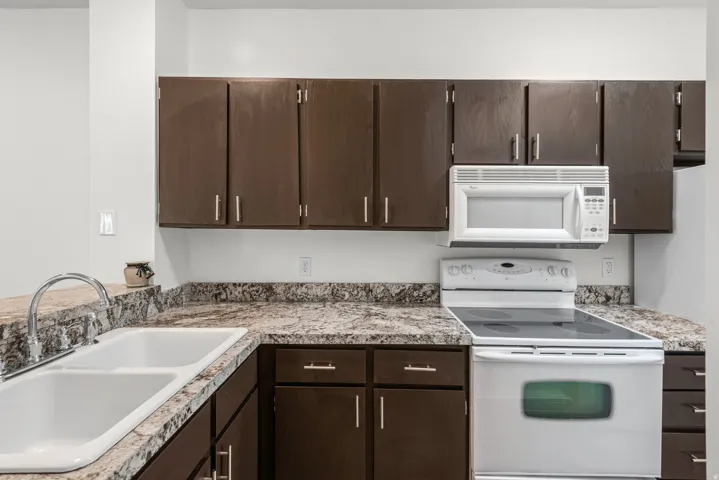 Fully renovated kitchen featuring dark wood cabinetry, white appliances, granite countertops, and LVP flooring.