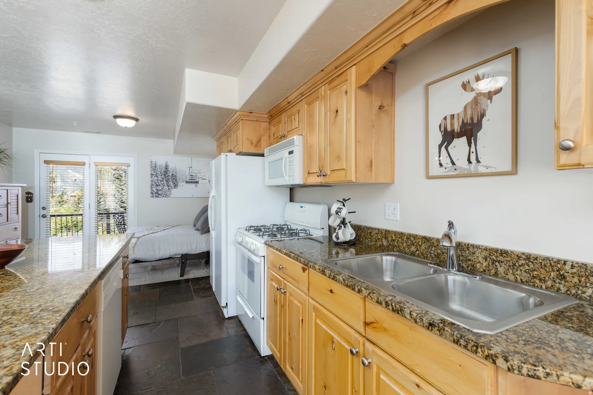 Wood-finish cabinetry with stone-finish countertops, dual stainless steel sink, and slate-finish flooring