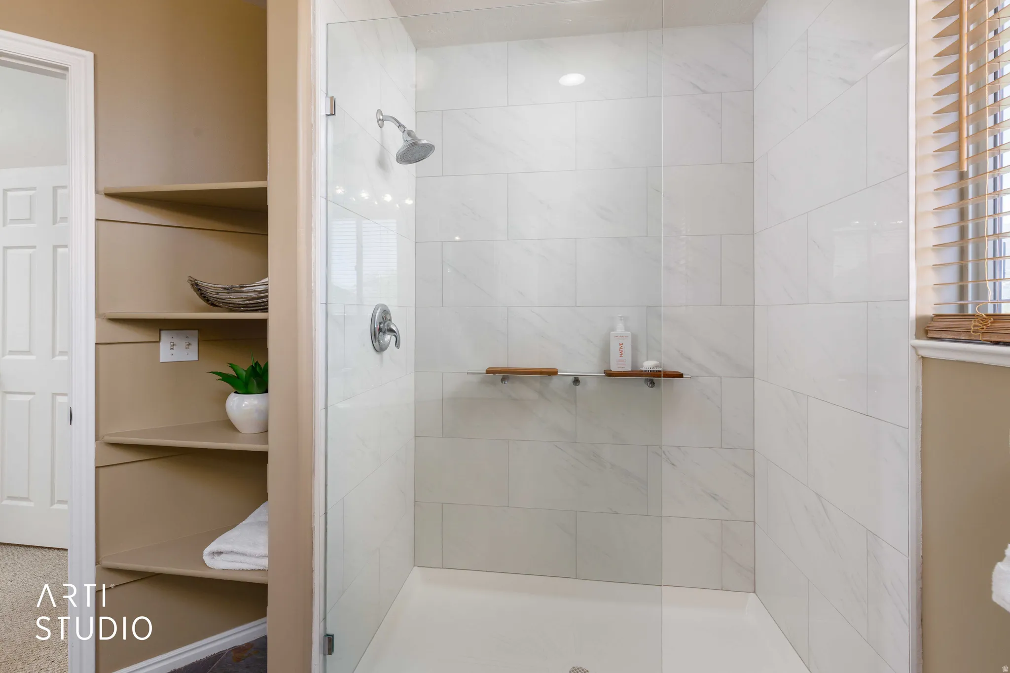 Newly renovated glass-enclosed shower with white tiled walls, a rain showerhead, and integrated shelving