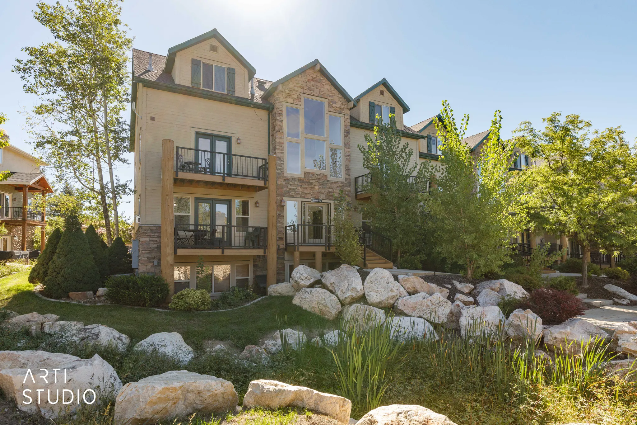 Unit 610 has the top-left balcony. Stone and siding exterior with multiple balconies, large windows, dormer windows, and a tiered rock garden