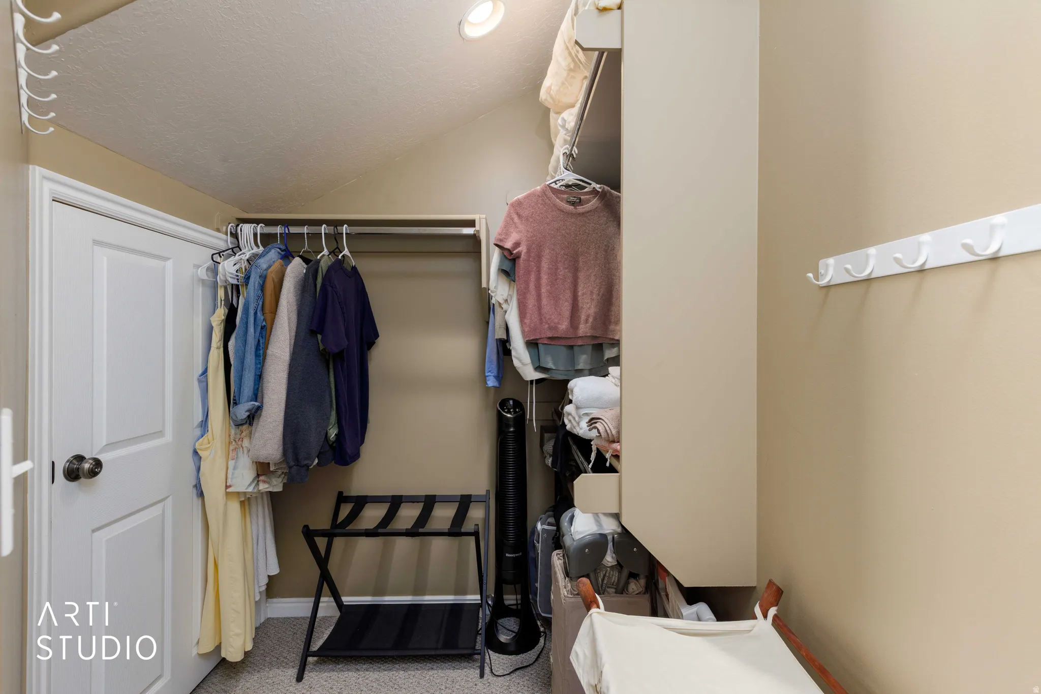 Sloped ceiling closet with a built-in hanging rod, recessed lighting, and wall-mounted hooks