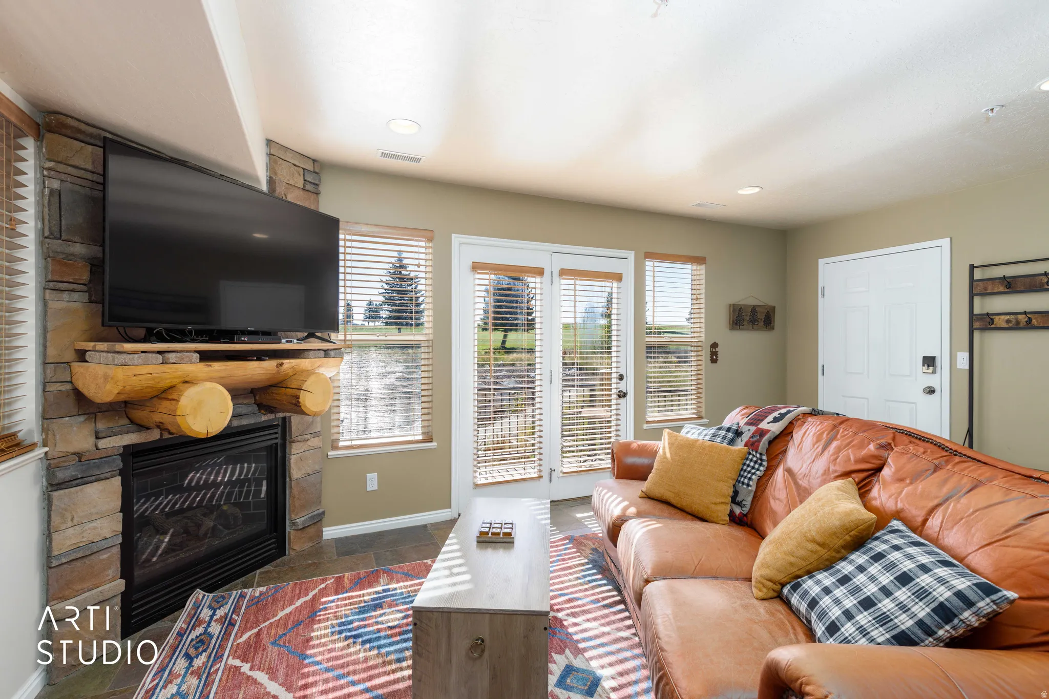 Stone-clad fireplace with a wood mantel, glass-front doors, and a built-in television. Sleeper sofa, balcony opens to view of golf course.