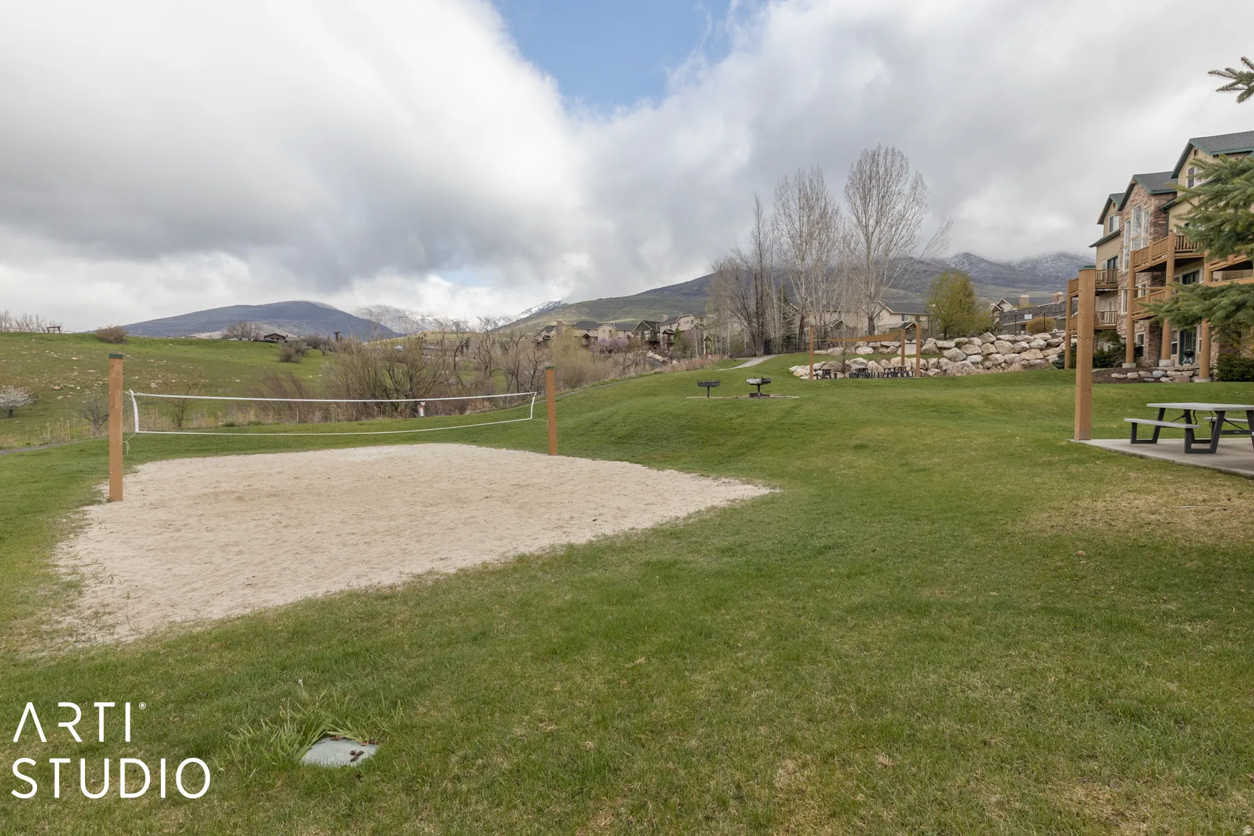 Sand volleyball court with a net, expansive lawn, and picnic area featuring a table and benches