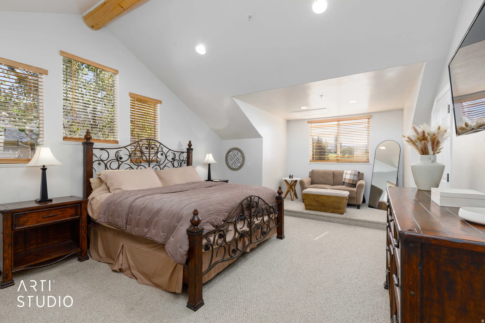 King bed. Vaulted ceiling with exposed wood beam, recessed lighting, and multiple windows with wood-finish blinds