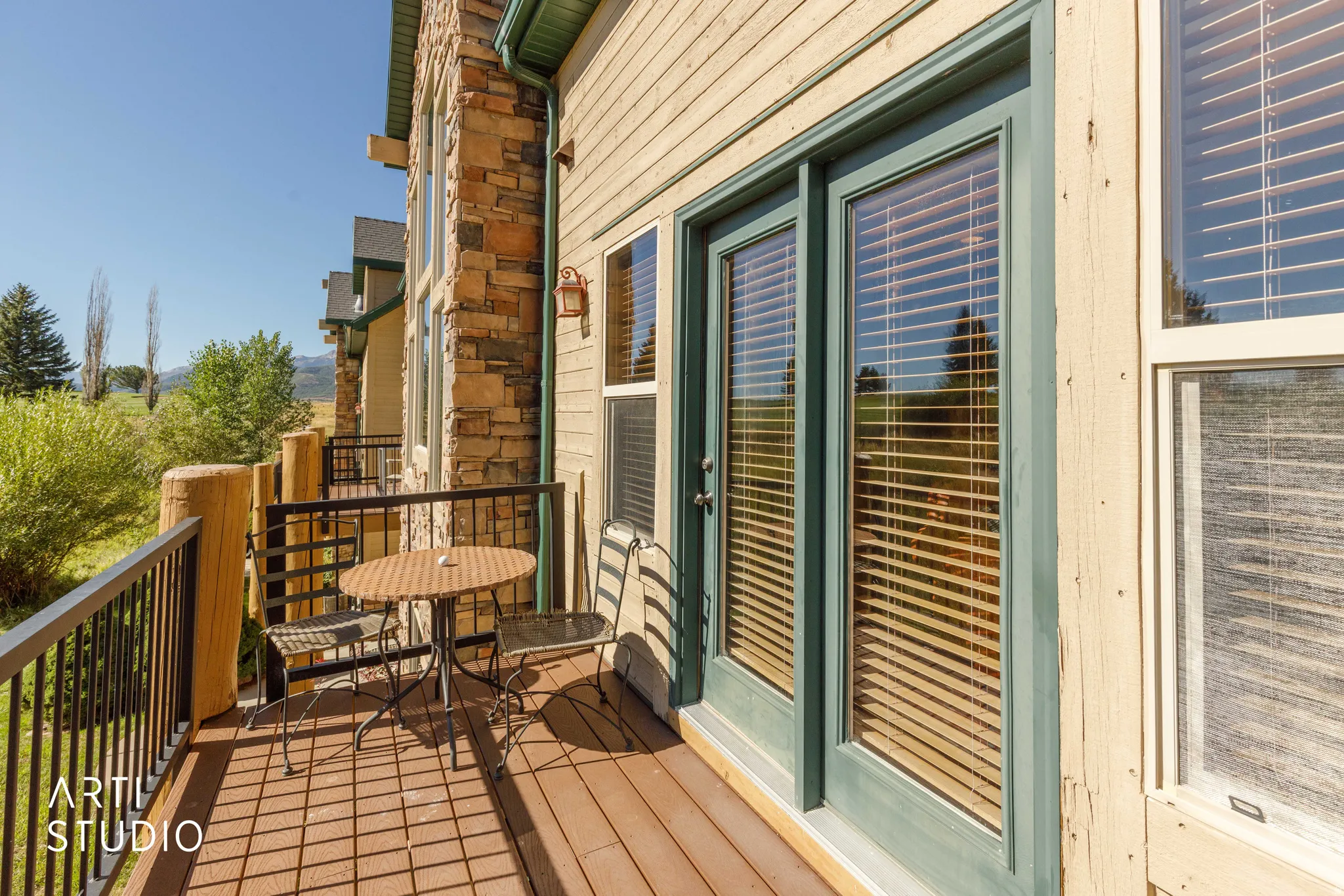 South balcony featuring wood-finish decking, black metal railings, and a stone facade