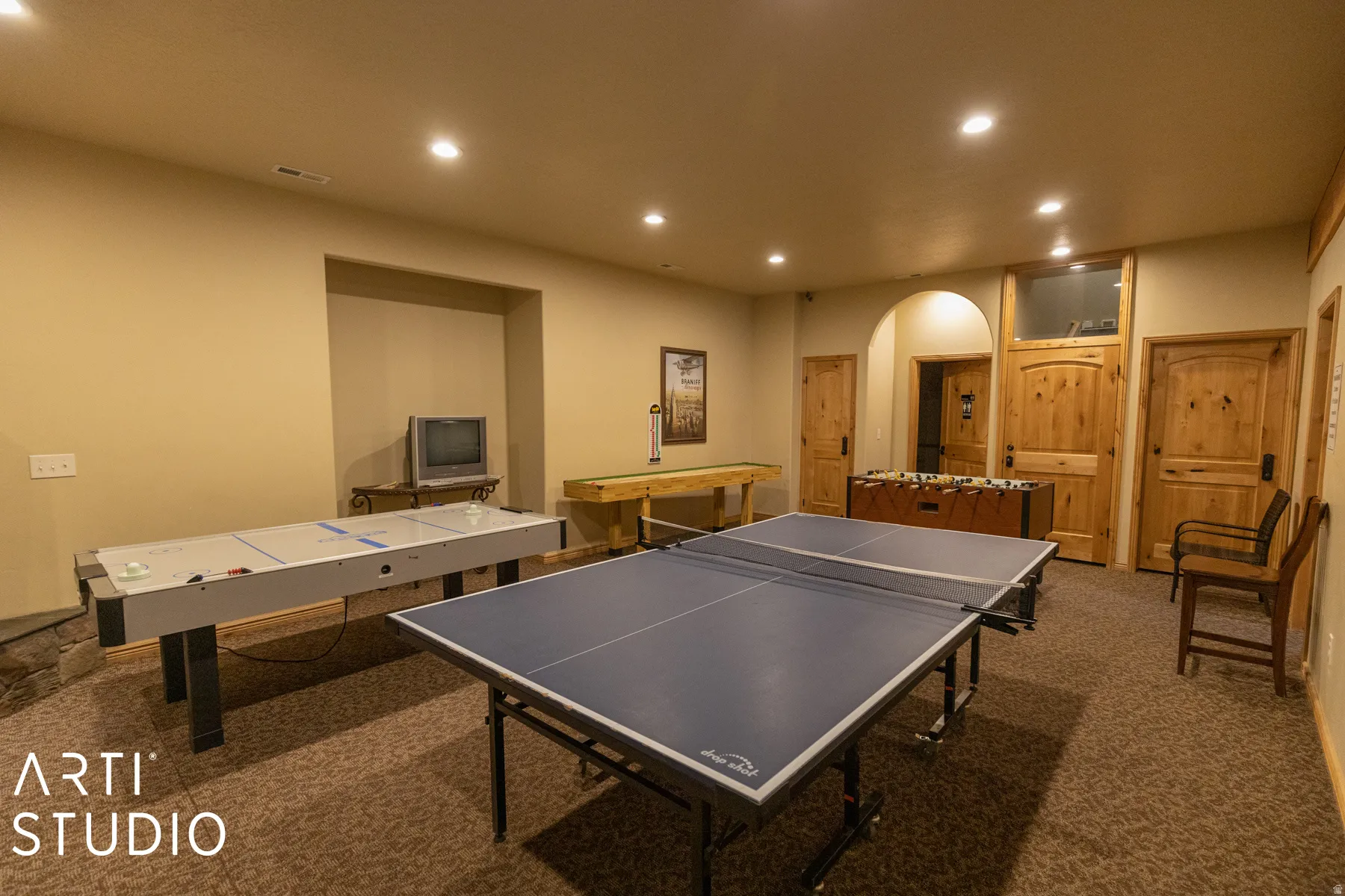 Recessed lighting illuminates the carpeted room, featuring multiple wood doors and an arched doorway