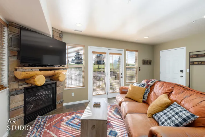 Stone-clad fireplace with a wood mantel, glass-front doors, and a built-in television. Sleeper sofa, balcony opens to view of golf course.