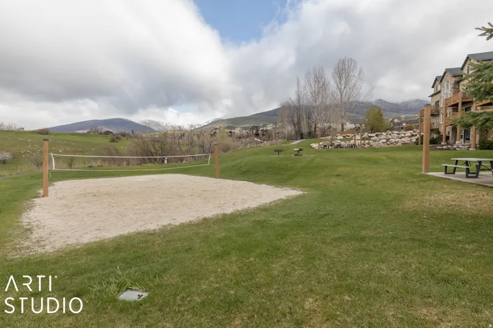 Sand volleyball court with a net, expansive lawn, and picnic area featuring a table and benches
