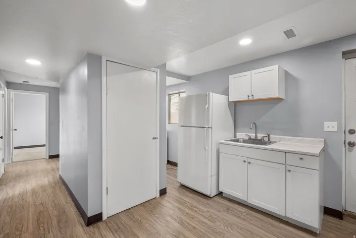 Kitchenette with white cabinetry, stainless steel sink, and refrigerator, featuring wood-finish flooring and recessed lighting