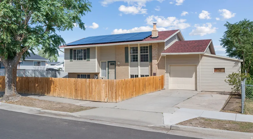 Split-level residence featuring solar panels, a wood privacy fence, attached garage, and a concrete driveway