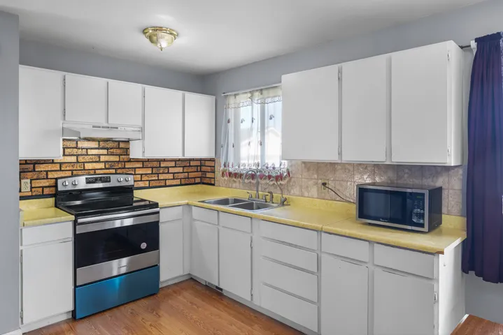 Kitchen featuring wood-finish flooring, white cabinetry, a double basin sink, and a tile backsplash