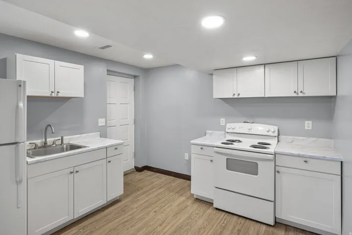 Kitchenette featuring white cabinetry, a stainless steel sink, a full-size white refrigerator, a white electric range, and wood-finish flooring