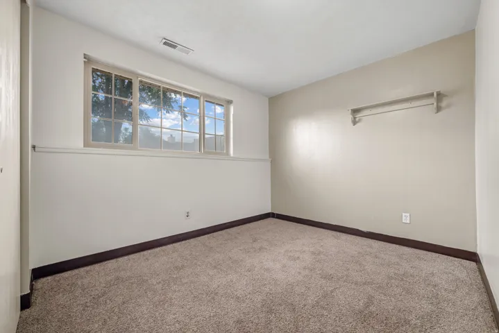 Carpeted room featuring a multi-pane window, neutral-toned walls, and a built-in shelf with hanging rod