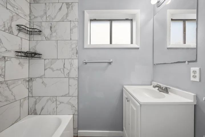 Bathtub with white subway tile surround, white vanity with integrated sink, and wall-mounted mirror