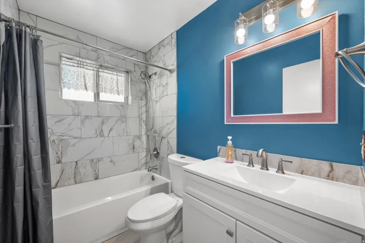 Bathtub with tiled surround, single vanity with integrated sink, chrome faucet, and overhead lighting fixture