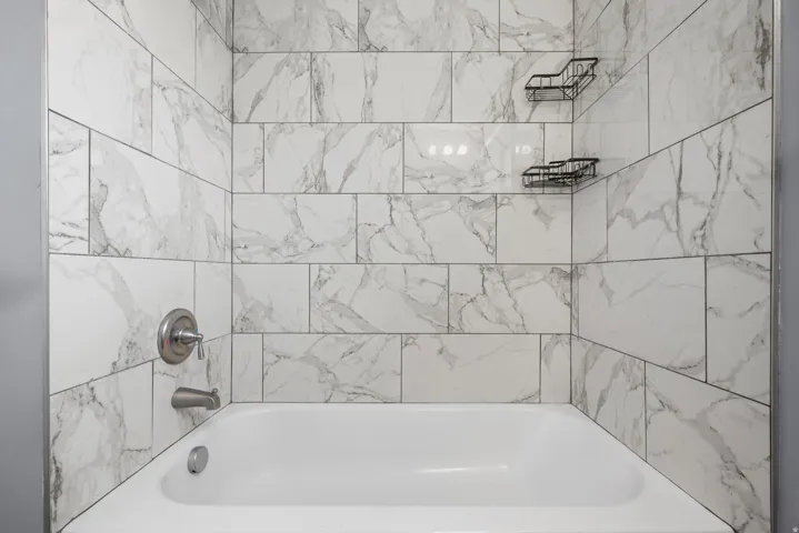 Bathtub with subway tile surround, brushed nickel fixtures, and built-in corner shelving