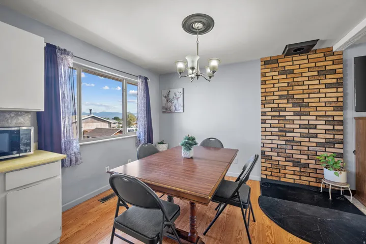 Brick wall accent with hearth, wood-finish flooring, and a multi-pane window