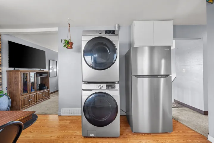 Wood-finish flooring with a stacked laundry system, stainless steel refrigerator, and upper white cabinetry