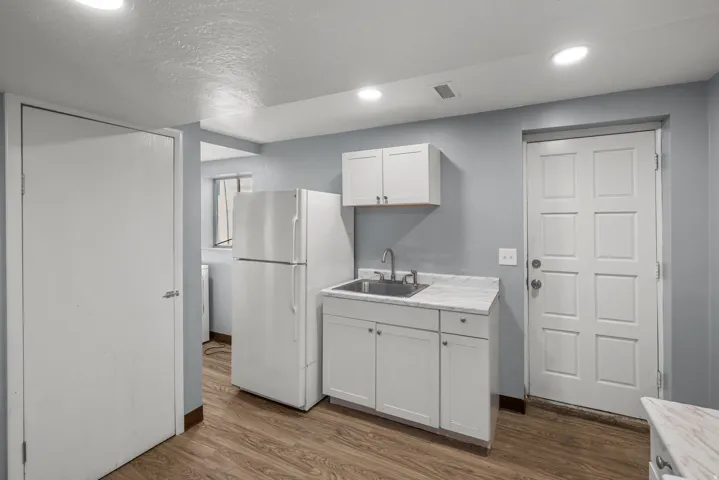Kitchenette featuring white cabinetry, a stainless steel sink, wood-finish flooring, and recessed lighting