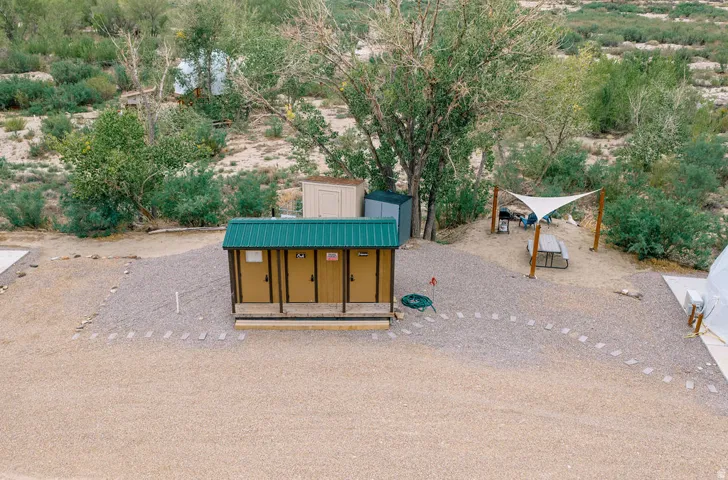 Gravel outdoor area with a utility building featuring a green metal roof, a shade sail structure, and a picnic table