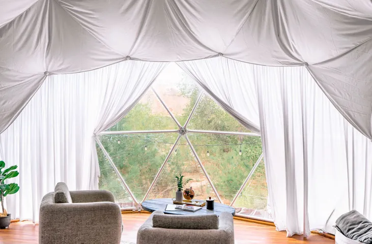 Geodesic dome structure featuring a large window wall, white fabric interior lining, and warm wood-finish flooring