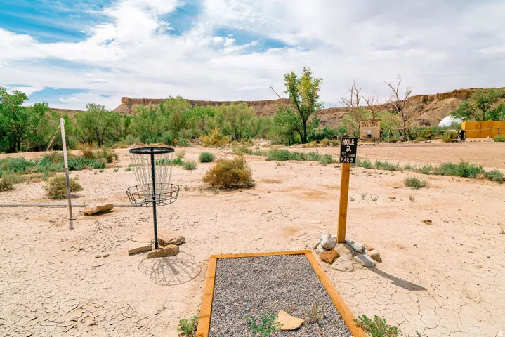 Disc golf course featuring a tee pad with gravel surface, metal basket, and directional signage