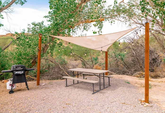 Gravel outdoor gathering space featuring a shade sail, string lighting, and wood posts