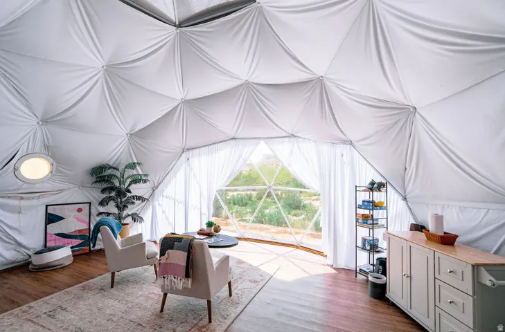 Geodesic dome interior featuring wood-finish flooring, a white fabric ceiling, expansive window openings, and a built-in cabinet with a wood-finish countertop