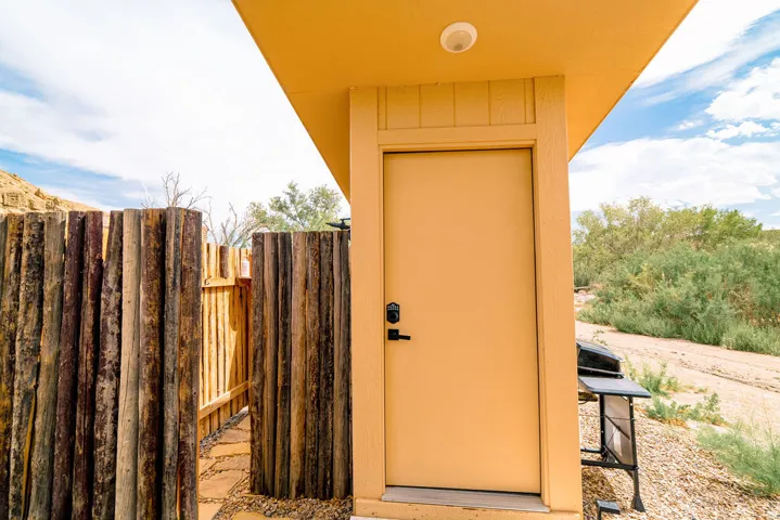 Private wood fence enclosure with a stone pathway, leading to a solid exterior door with a black handle