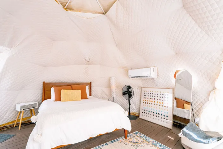 Dome structure with quilted wall coverings, wood-finish flooring, a wood-frame bed, and a wall-mounted air conditioning unit