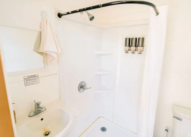Compact shower with white surround, built-in corner shelving, and a curved shower rod