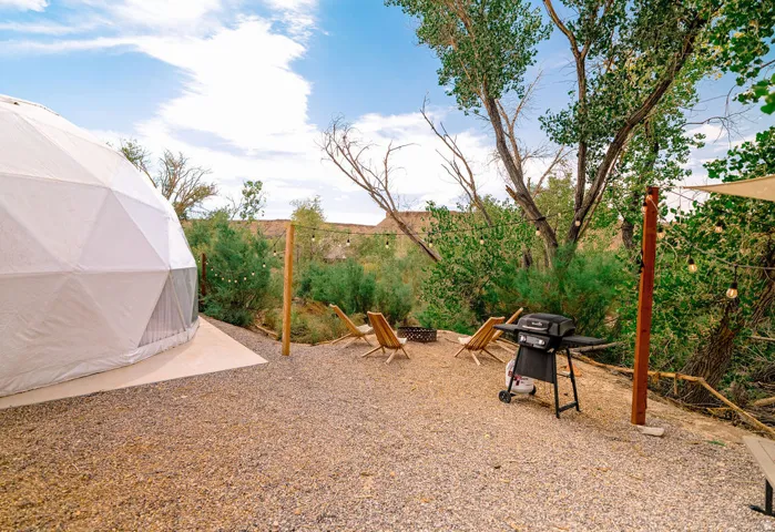 Geodesic dome structure with a gravel patio, featuring a fire pit area with wooden chairs, and string lighting