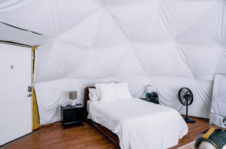Dome-style interior with white fabric paneling, wood-finish flooring, and a white paneled door with a deadbolt