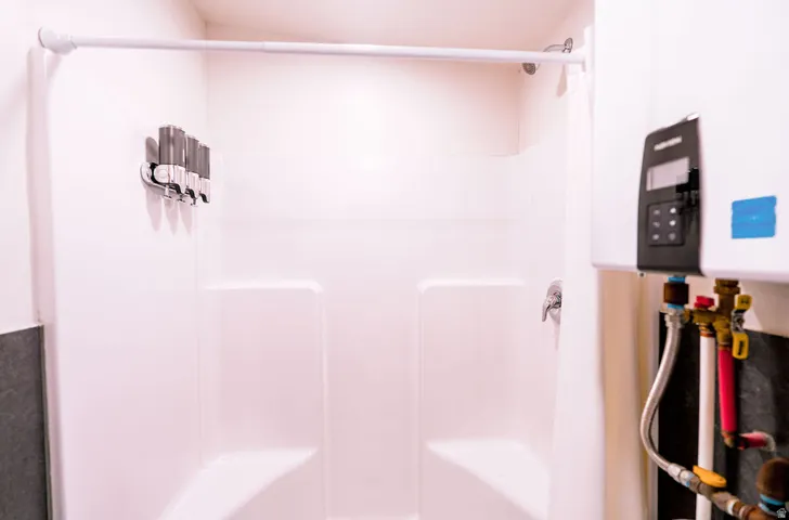 White shower stall with built-in shelving, chrome fixtures, and a shower curtain rod