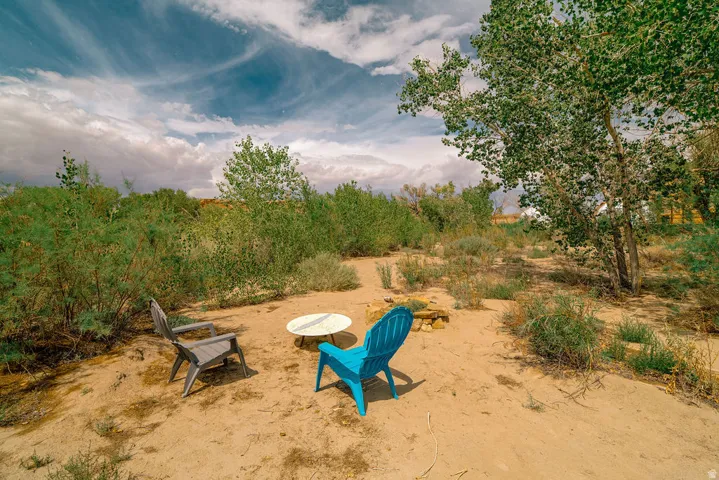 Sand-covered ground with a fire pit area, surrounded by low-growing vegetation and mature trees