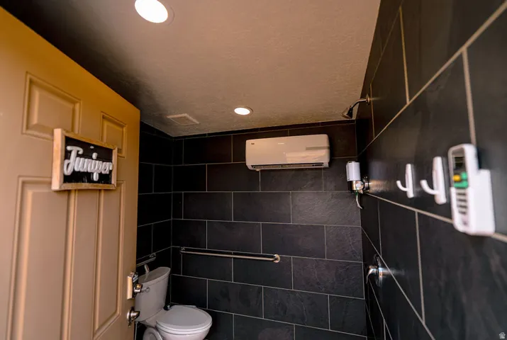 Recessed ceiling lighting, dark tile wall finishes, grab bar, and a wall-mounted mini-split unit