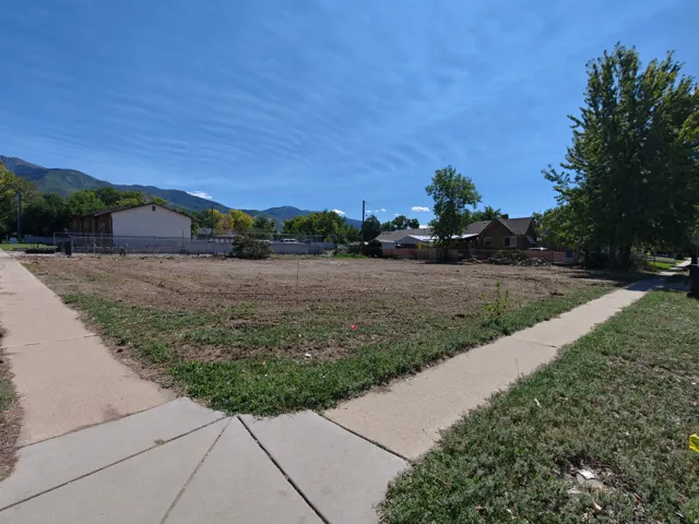 Expansive cleared lot with mature trees, established sidewalks, and distant mountain scenery